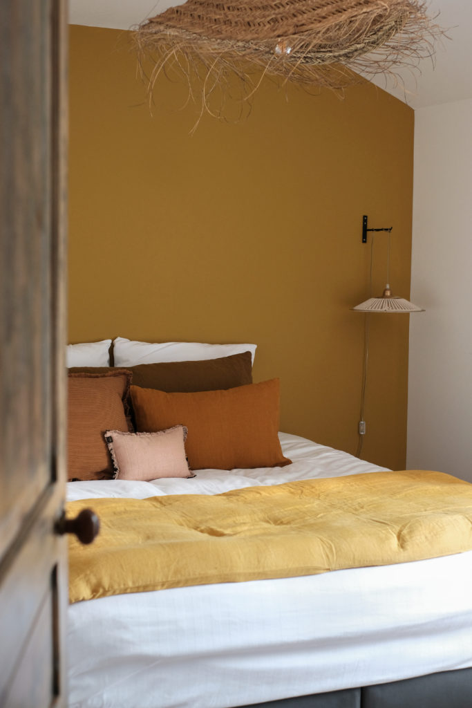 Chambre avec peinture jaune, et lit double composé de coussins marrons et blancs